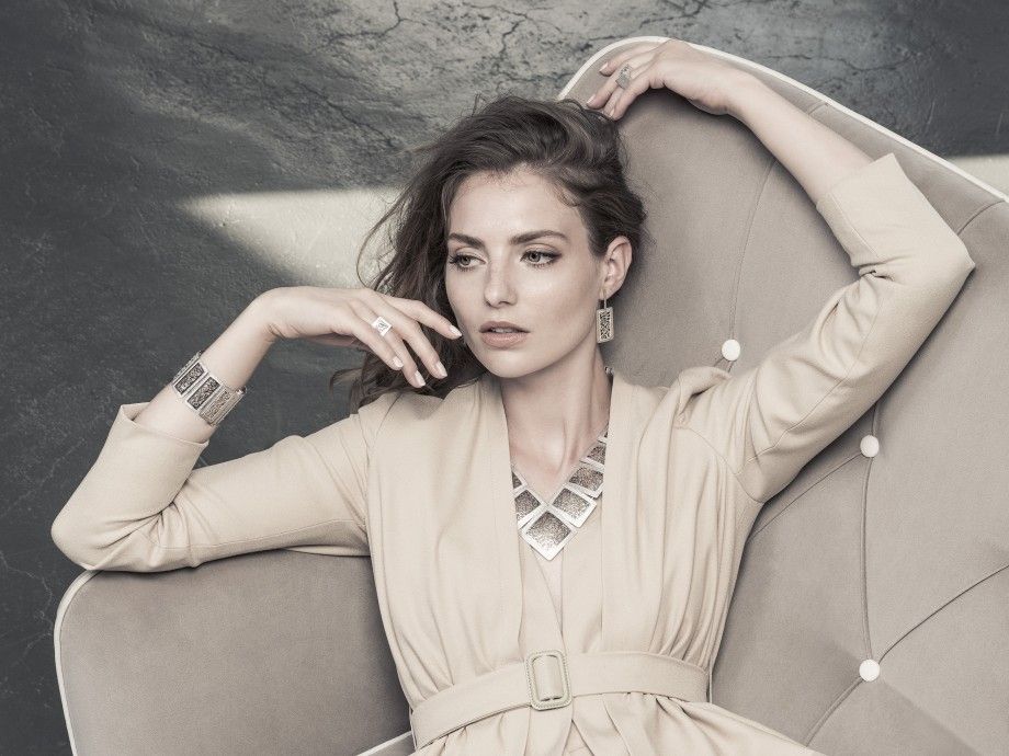 Mulher elegante reclinada usando anel hedra feminino da Topázio 1874 com colar geométrico e bracelete em prata