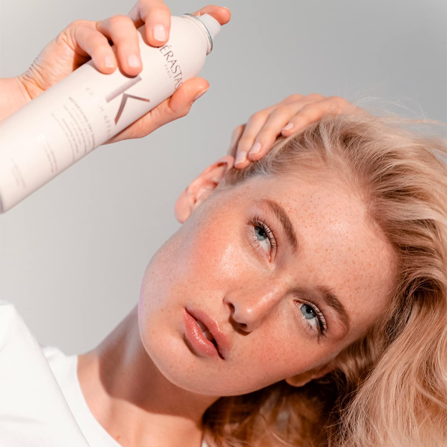 Mulher aplicando spray de produtos Kerastase online para cuidado e tratamento de cabelo moderno e saudável