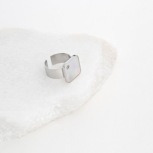 anel ajustável aço quadrado prateado com pedra discreta e design minimalista da Carmo Joalheiros sobre base de mármore branco