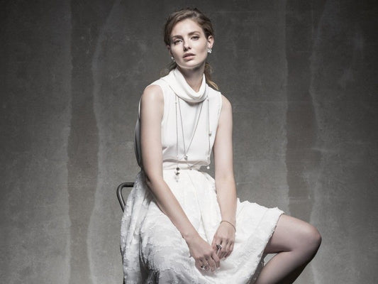 Mulher elegantemente vestida em vestido branco com joias Carmo Joalheiros mostrando pulseira feminina fuji delicada no pulso