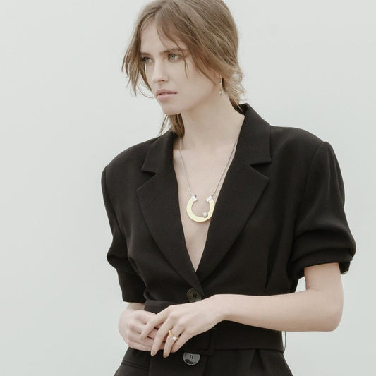 Modelo de blazer preto mostrando anel orbit dourado da Topazio 1874 com colar moderno