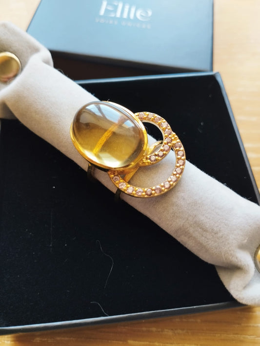 Anel dourado ELITE com cabochão âmbar oval e dois círculos cravejados mostrado em estojo joia exclusiva Elite Anel Moon GreenGold